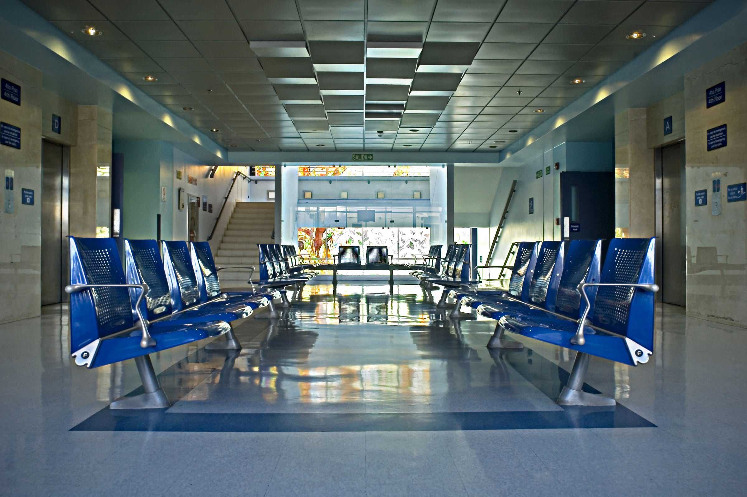 Sala de espera de la Clínica Bíblica con bancas azules en fila