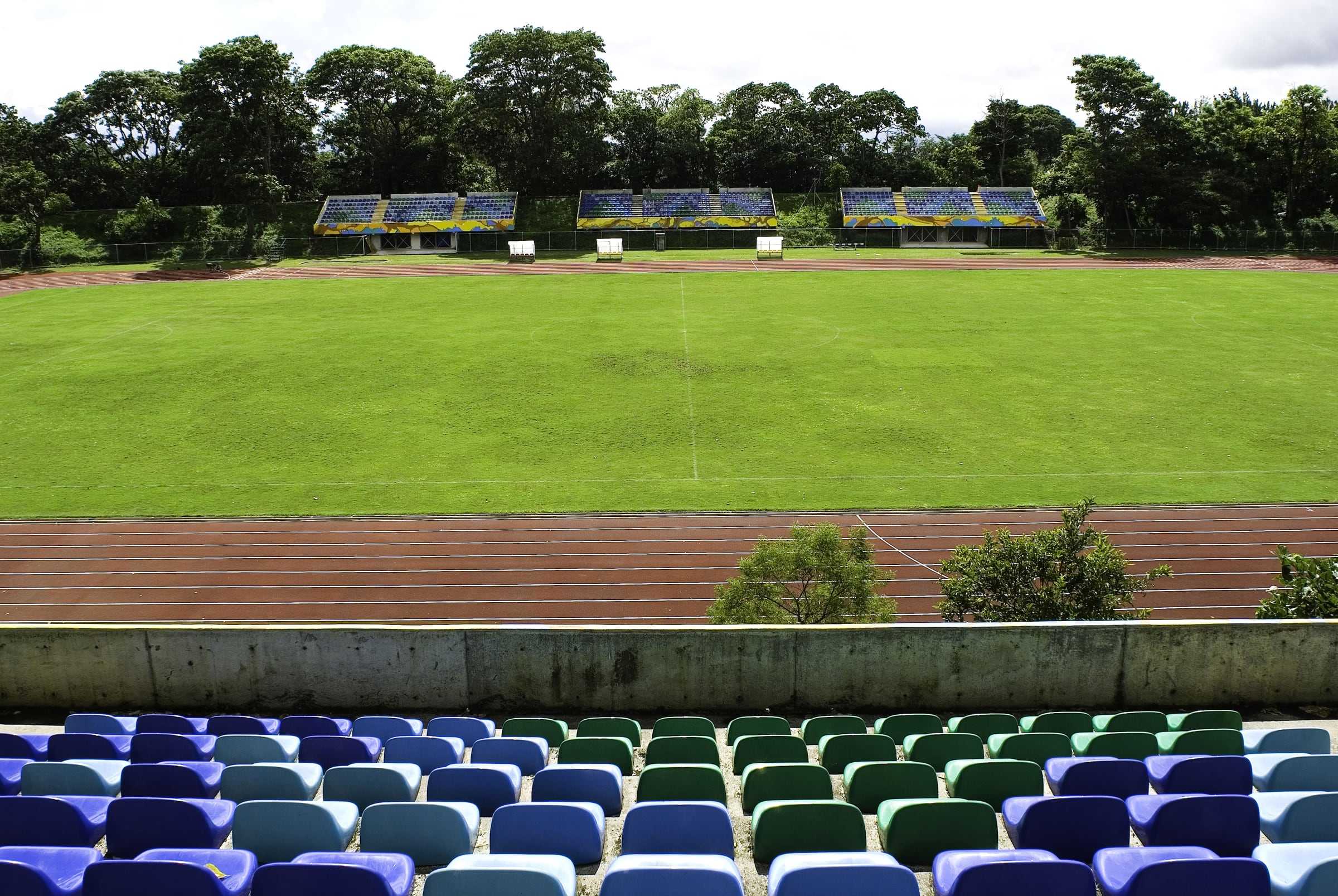 Cancha del Estadio Ecológico de la UCR con las graderías de butacas de colores al fondo